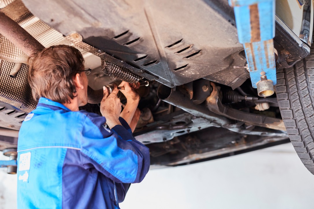 PKW-Service und Reparatur bei Albert Tycho Kruse in Minden Mechaniker arbeitet unter einem angehobenen PKW an der Fahrzeugunterseite