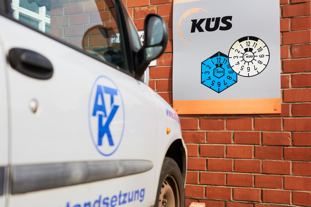 Haupt- und Abgasuntersuchung für PKW bei Albert Tycho Kruse in Minden Hinweistafel zur Hauptuntersuchung an einer Werkstattfassade mit geparktem Fahrzeug