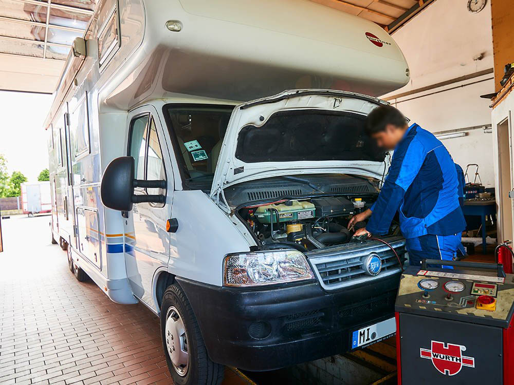 Wohnmobil-Service und Reparatur bei Albert Tycho Kruse in Minden Wohnmobil steht in einer Werkstatt mit geöffnetem Motorraum, Mechaniker arbeitet am Fahrzeug