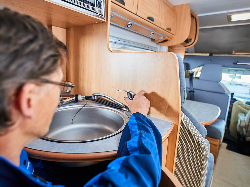 Service für Küche und Sanitär im Wohnmobil bei Albert Tycho Kruse in Minden Mechaniker arbeitet am Spülbecken in der Küche eines Wohnmobils