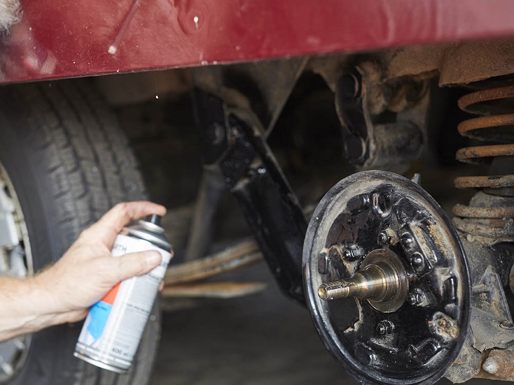 Wartung und Instandsetzung von Fahrwerkskomponenten bei Nutzfahrzeugen in Minden Hand sprüht Schmiermittel auf eine Achskomponente eines Nutzfahrzeugs